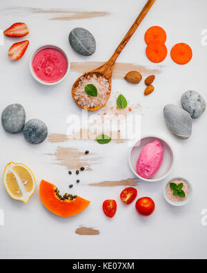 Hausgemachte Hautpflege und Körperpeelings mit roten natürliche Zutaten Erdbeeren, Tomaten, Himalaya-Salz, Papaya, Karotte und Stein auf weißem Holz- backgrou Stockfoto