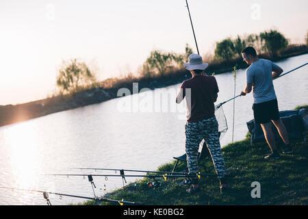 Junger Mann angeln an einem See bei Sonnenuntergang und genießen Hobby Stockfoto