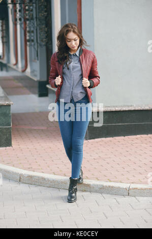 Junge schöne stilvolle Frau in Jacke ein Burgunder Pilot und blaue Jeans, street style, Frühling und Herbst trend, Aussehen, Haare im Wind Stockfoto