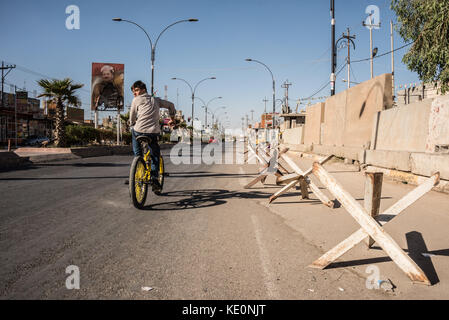 Kirkuk, Irak. 17 Okt, 2017. Ein Junge Zyklen durch die in der Nähe der verlassenen Kurdischen Viertel von Kirkuk, Vergangenheit ein Poster von Barzani, die während des Konflikts in den letzten 48 Stunden gebrannt wurde. Kirkuk, Irak, 17. Oktober 2017 Credit: Elizabeth Fitt/Alamy leben Nachrichten Stockfoto