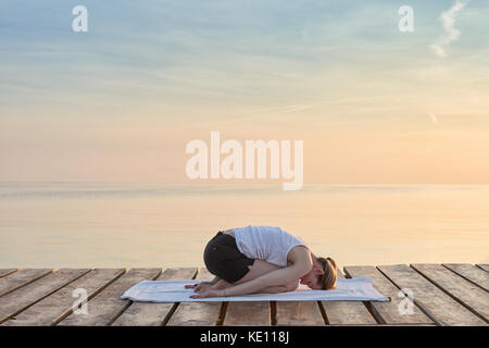 Ansicht der Rückseite des junge Frau saß auf dem Handtuch Üben Yoga von Meer bei Sonnenuntergang Stockfoto