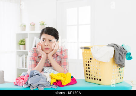 Unglücklich attraktive Frau maid Falten Kleidung Langeweile und lehnte sich auf unordentliche Kleidung träumen, wenn sie in viele allgemeine Ordnung und Sauberkeit zu Hause. Stockfoto