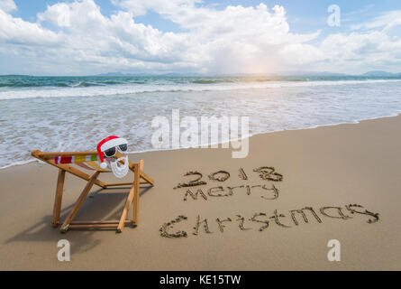 2018 Frohe Weihnachten in Sand geschrieben mit Liegestuhl am tropischen Strand. Stockfoto