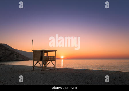 Orange und lila Sonnenuntergang über Ile Rousse hinter einem hölzernen lifeguard Tower auf einer verlassenen Ostriconi Strand in der Balagne Korsika Stockfoto