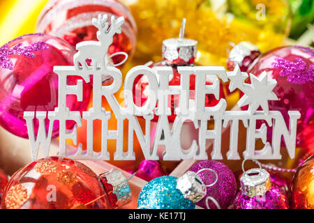 Christbaumkugeln in verschiedenen leuchtenden Farben als Hintergrund, frohe Weihnachten Frohe Weihnachten übersetzt Stockfoto