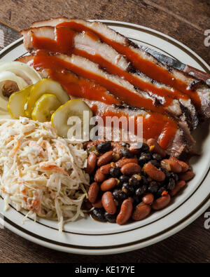 Einen Teller mit geschnittenem Bruststück mit gebackenen Bohnen, cole slaw und Dill Pickles auf rustikalen Hintergrund Stockfoto