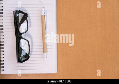 Kugelschreiber, leer Notebook, Brillen auf Holz Büro Schreibtisch. Business, Bildung Konzept. Ansicht von oben mit der Kopie Raum. Selektive konzentrieren. Stockfoto