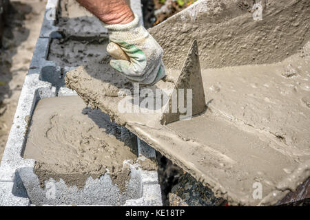 Nahaufnahme von Mason hand Gießen aus Mörtel in Beton Schalung Blocks von Rad - barrow Stockfoto