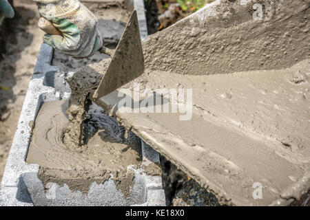 Nahaufnahme von Mason hand Gießen aus Mörtel in Beton Schalung Blocks von Rad - barrow Stockfoto