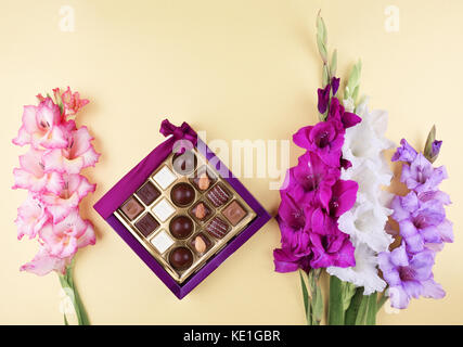 Wunderschöne gladiolen Blumen auf Gelb mit köstlichen Pralinen in Geschenkbox. Stockfoto