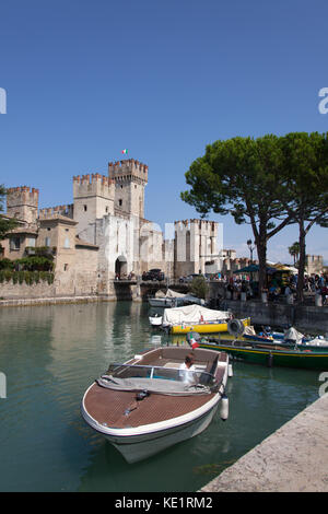 Sirmione, Italien. malerischen Blick auf eine touristische Bootsfahrt in den Burggraben der Scaliger Burg, mit der Burg Eingang im Hintergrund. Stockfoto