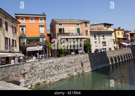 Sirmione, Italien. Malerischer Blick auf den Graben der Scaliger Burg, mit Geschäften und Restaurants auf der Via Dante im Hintergrund. Stockfoto