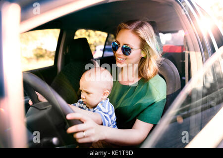 Junge Mutter mit ihrem kleinen Sohn im Auto. Eine Frau und Baby boy vorgibt, zu fahren. Stockfoto