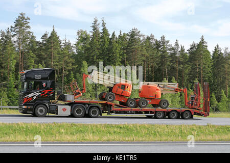 Paimio, Finnland - Juni 3, 2016: schwarz SCANIA LKW-Transporte zwei Hubarbeitsbühnen auf lowboy Trailer entlang der Autobahn im Süden Finnlands. Stockfoto