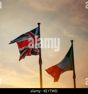 Italienische und britische Flagge auf einer Stange im Sonnenuntergang, zwei Nationale Fahnen von Italien und dem Vereinigten Königreich (Großbritannien) winken in den Wind. Stockfoto
