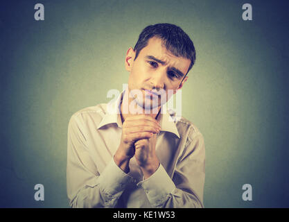 Closeup Portrait von verzweifelten jungen Mann mit gefalteten Händen, bitte vergib mir auf grauen Hintergrund. Menschliche emotion Gesichtsausdruck Gebühr Stockfoto