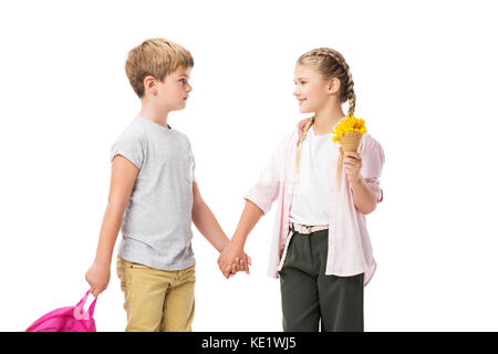 Happy adorable Kinder holding Rucksack und gelbe Blumen, während zusammen und halten sich an den Händen auf Weiß isoliert Stockfoto