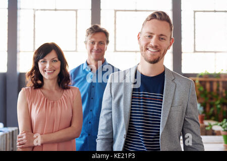 Porträt einer selbstbewussten jungen Geschäftsmann in einem modernen Büro mit zwei lächelnde Arbeit Kollegen hinter ihm im Hintergrund Stockfoto