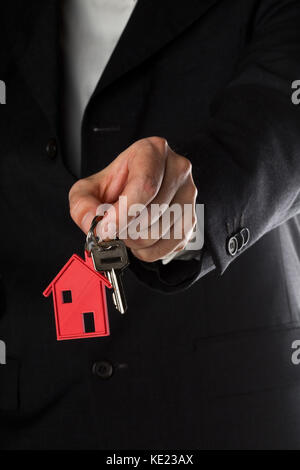 Mann in Anzug holding Haus Tür Schlüssel mit roten Haus Schlüsselanhänger Anhänger Stockfoto