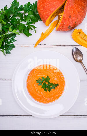 Kürbis Suppe pürieren, in eine runde weiße Platte und frische Kürbis auf weißem Holz- Tabelle, Ansicht von oben Stockfoto