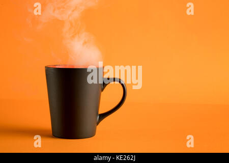 Schwarz Kaffee Tasse mit Dampf auf orange Hintergrund. sparse Zusammensetzung Stockfoto