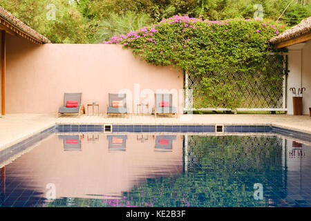 Drei Sessel sowie ein Schwimmbad, Badetücher, versteckt durch die Vegetation an der Wand im Boutique Hotel, Tangalle, Sri Lanka. Stockfoto