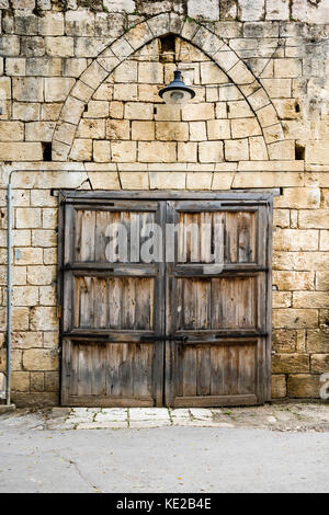 Doppelflügelige Tür mit rostiges Metall Bars, geschlossen, in limetone Wand mit Steinbogen in Batroun, Libanon. Stockfoto