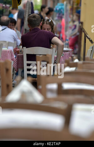 Ein junges Paar, das Essen in einer typisch griechischen Taverne in einer belebten Straße in der Altstadt von kerkira in Korfu in Griechenland an einem Tisch sitzen. Stockfoto