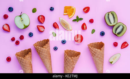 Kegel und bunten verschiedene Früchte Himbeere, Heidelbeere, Erdbeere, Orange Slice, halbierte Kiwi, Apfel, Tomate und Pfefferminze Blätter setup auf Rosa hinterg Stockfoto