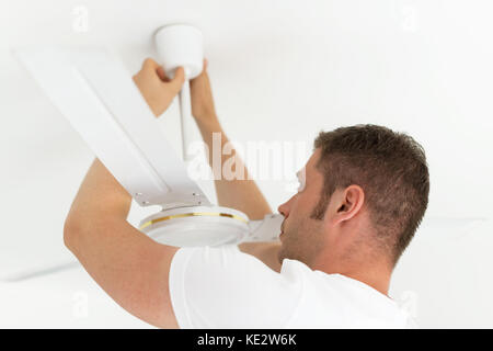Männlicher Techniker, der den Deckenventilator installiert. Stockfoto