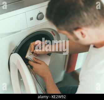 Männlicher Techniker, der die Waschmaschine repariert und den Herstellercode schreibt. Stockfoto