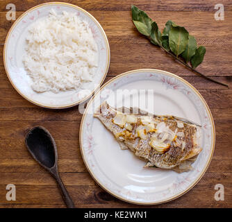 Ofen zubereitet ganze Fische, mit Knoblauch und Zwiebel in Scheiben geschnitten, auf weißem Porzellan dekorative Platte und einen Teller mit weißer Reis auf einem hellen Hintergrund Stockfoto