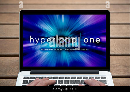 Die Hyperloop ein Logo wird auf dem Bildschirm des MacBook Pro Laptop gezeigt, Schuß gegen eine Holzbank einschließlich der Finger des Mannes (nur redaktionell). Stockfoto