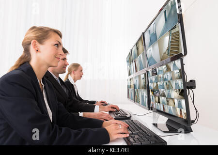 Weibliche und männliche Security system Operatoren auf CCTV-Aufnahmen auf mehreren Computern Stockfoto