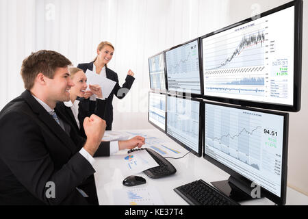 Glücklich, aufgeregt, männlichen und weiblichen Börse Broker in Diagrammen auf mehrere Computer suchen Stockfoto