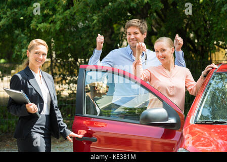 Gerne weibliche Händler stehen neben Paar zeigen Schlüssel neu gekaufte Auto Stockfoto