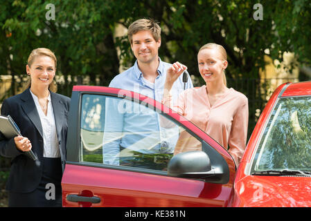 Händler stehen neben glückliches junges Paar mit Schlüssel neu gekaufte Auto Stockfoto
