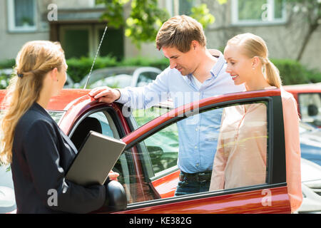 Verkäuferin stehen neben Paar an der neuen roten Auto suchen Stockfoto