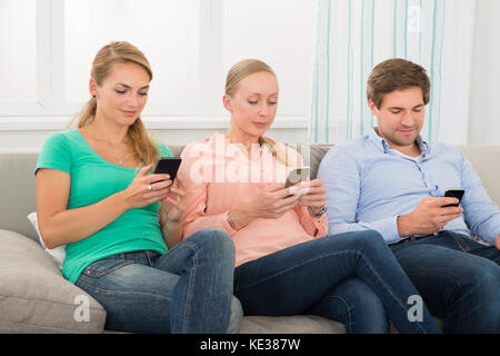 Gruppe von Menschen sitzen auf einem Sofa mit Handy zu Hause Stockfoto