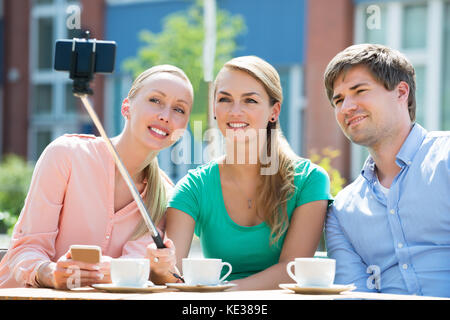 Glückliche junge Freunde unter Selfie mit selfie Stick im Cafe Stockfoto