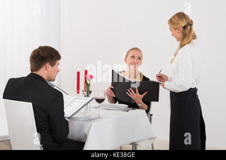 Weibliche Bedienung, einen Auftrag von einem glücklichen Paar im Restaurant Stockfoto