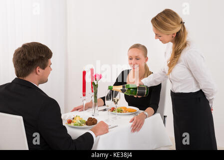 Weibliche Bedienung in Gießen Champagner Glas für glückliches junges Paar im Restaurant Stockfoto