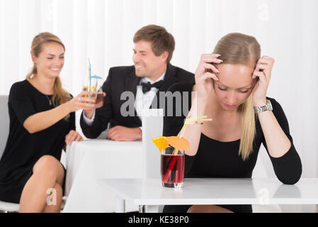 Deprimiert Frau sitzt im Restaurant Vor Paar Toasten Glas Cocktails Stockfoto