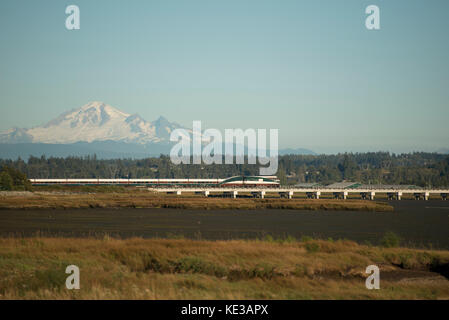 Amtrak Cascades Zug passiert Schlamm Bucht mit Mount Baker in Surrey, BC, Kanada Stockfoto