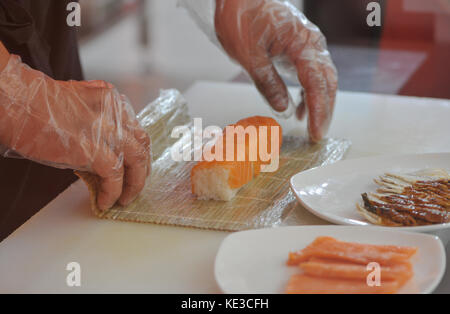 Der Koch bereitet Sushi, durch Drehen der Rollen. Nahaufnahme der Hand der Koch bereitet Sushi in einem Fast-Food-Restaurant Stockfoto