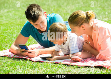 Glückliche Eltern zur Festlegung im Park mit Blick auf Seinen Sohn mit Smartphone Stockfoto