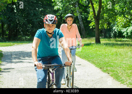 Junge lächelnde Paar genießt die Fahrt mit dem Fahrrad Im Park Stockfoto