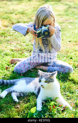 Kind Mädchen Fotografieren einer Katze, die auf dem Gras draussen im Garten. Stockfoto