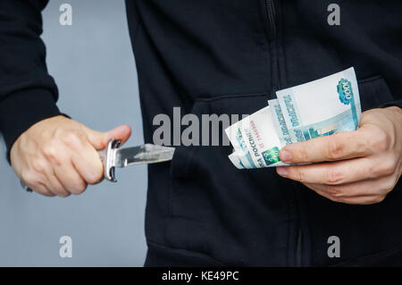 Räuber mit Messer in der Hand und russische Geld. Bandit zieht seine Pocket Taschenmesser auf Bedrohungen. ein Räuber mit einem Messer in der Hoodie. Das Konzept der Stockfoto