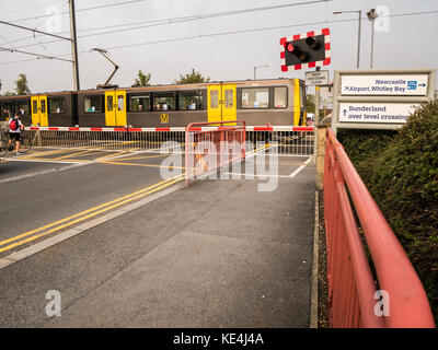 Eine elektrische Zug fährt entlang der Strecke über die Straße überqueren der Tyne und Wear metro bei East Boldon, England. Stockfoto